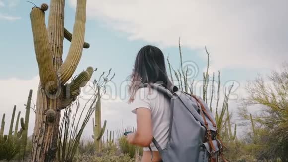 慢动作后景年轻兴奋的女游客与背包拍摄智能手机照片的大萨瓜罗沙漠仙人掌视频的预览图