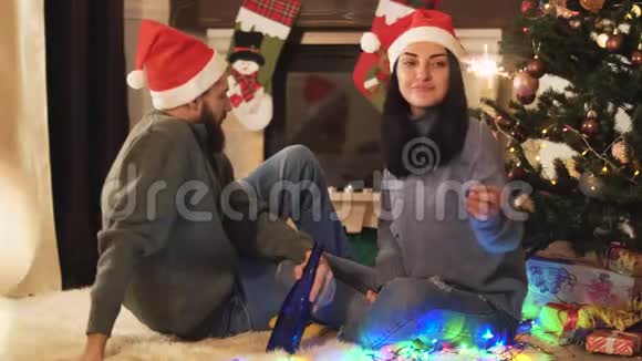 男人和女人坐在圣诞树附近女人手里拿着火花他拿着酒精瓶闪氏烧伤视频的预览图