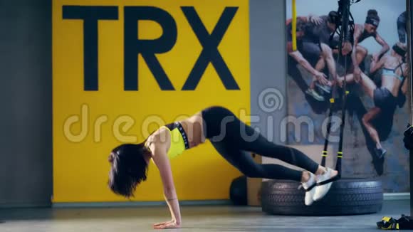 漂亮的黑发女人穿着紧身裤黄色上衣和运动鞋在TRX环上做运动在健身房里做陷阱视频的预览图