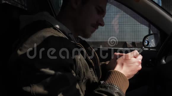 秋天的时候一个穿着皮夹克的男人坐在车里时使用智能手机视频的预览图