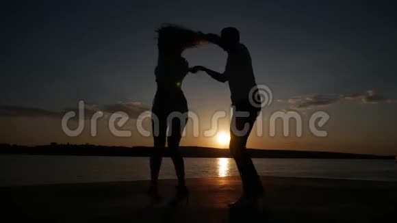 小男孩和小女孩在湖边日落时跳舞剪影拍摄视频的预览图