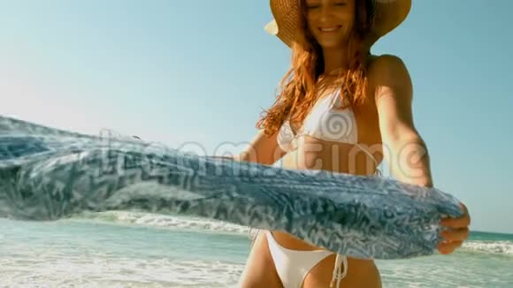 穿比基尼戴帽子的白种人年轻女子在阳光下沙滩上玩围巾视频的预览图