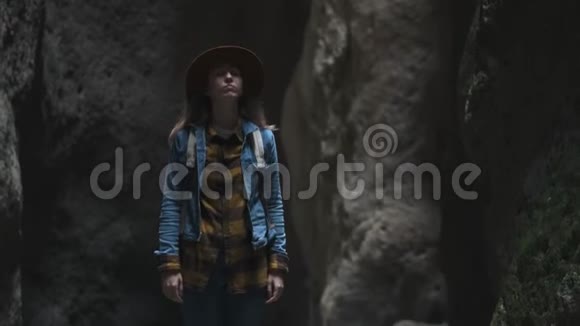 洞穴或峡谷中的女旅行者她戴着一顶帽子和一件夹克有一个背包探索一个古老的洞穴视频的预览图