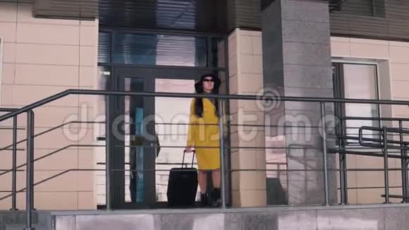 穿着黄色雨衣戴着帽子的一头深色长发的漂亮女人在酒店的门廊上走了出来视频的预览图
