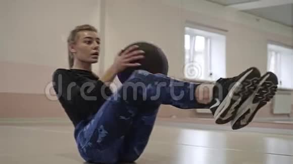 酷女孩在健身房里坐在地板上做运动把球从一边扔到另一边视频的预览图
