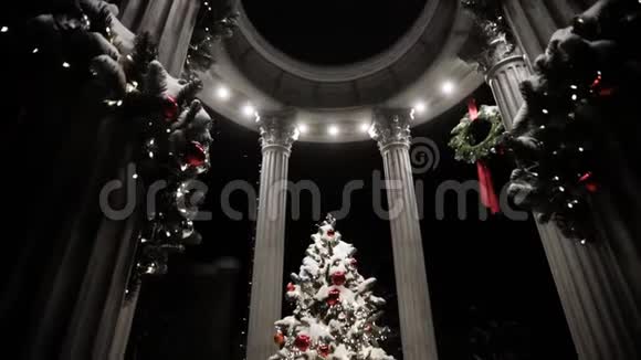 在神圣的夜晚用柱子覆盖着雪装饰在凉亭里的圣诞树视频的预览图
