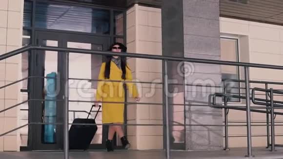 一位身穿黄色斗篷戴着帽子留着深色长发从酒店的门廊走出来摘下眼镜视频的预览图