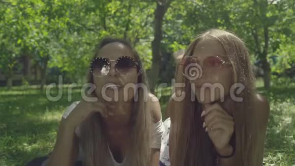 两个戴墨镜的年轻美女躺在绿草上视频的预览图