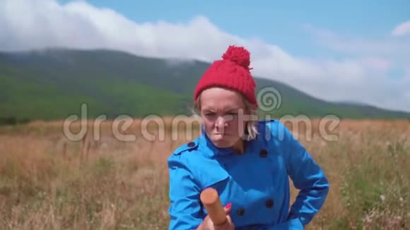 金发女郎玩得很开心站在一件蓝色的外套红色的帽子和杂耍或者用她的手抛出一个木棍视频的预览图