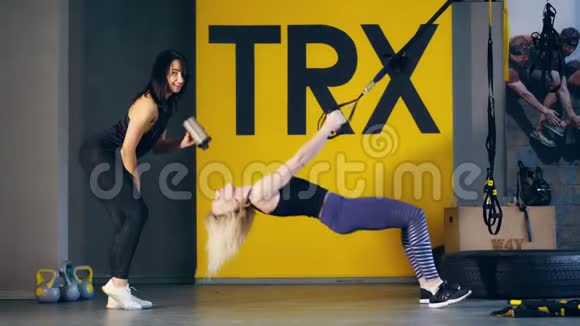 两位穿着紧身裤上衣和运动鞋的金发美女和深黑色美女在TRX循环陷阱和视频的预览图