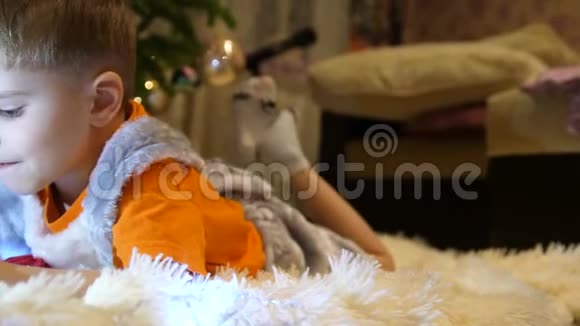 孩子躺在孩子们房间里柔软白色毯子上他正在智能手机上看动画片圣诞节视频的预览图