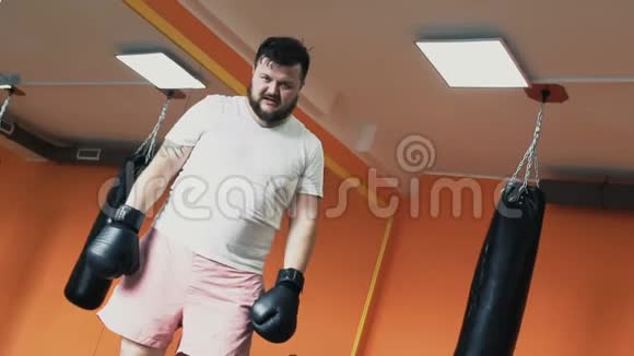 一个戴着手套的胖汗家伙在健身房训练拳击后累了丰满男子个人减肥演习与工作视频的预览图