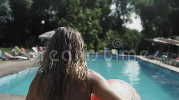 暑假一个带充气橡胶圈的年轻女子跳进了清澈的蓝色游泳池里视频的预览图