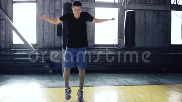 穿着黑色T恤和蓝色短裤的白人男子在原地跳跃时伸展手臂年轻运动员热身视频的预览图
