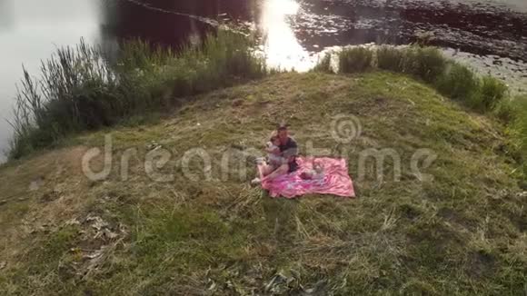 空中年轻的母亲和她的女婴在公园野餐家庭价值观温暖的颜色夏季现场无人机视频的预览图