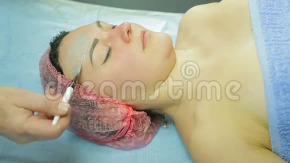戴手套的女性美容师用刷子把治疗面具涂在男人的脸上侧视视频的预览图