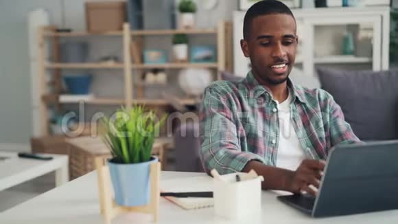 非裔美国人在家工作时使用笔记本电脑打字然后在纸上做笔记坐在办公桌前喝酒视频的预览图