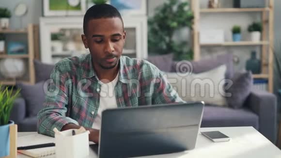 疲惫的美国黑人自由职业者正在使用笔记本电脑写在纸上然后感到头痛按摩他的身体视频的预览图