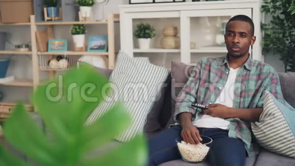 无聊的非裔美国人正在电视上看无聊的电影吃爆米花拿着遥控器有人坐着视频的预览图