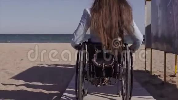 轮椅上的年轻残疾妇女在春季或春季在靠近海边的木制坡道旁为残疾人移动视频的预览图