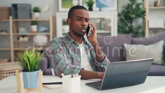 不快乐的非裔美国自由职业者正在用手机表达负面情绪并使用笔记本电脑工作视频的预览图