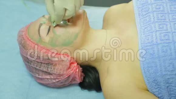 戴手套的美容师用棉垫从女人的脸上摘下一个粘土面具侧视图视频的预览图