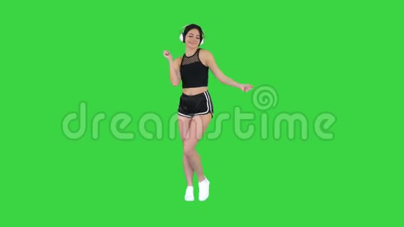 年轻快乐的运动女性听着耳机里的音乐在绿色屏幕上跳舞Chroma键视频的预览图