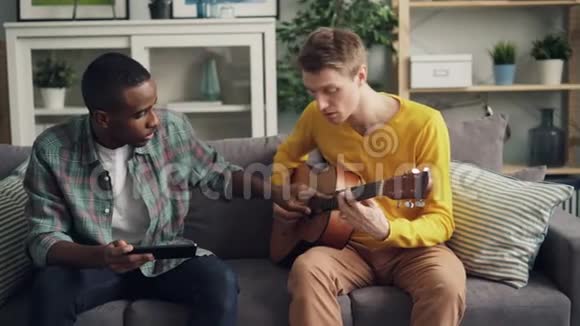 非裔美国人用平板电脑教他的高加索朋友一起弹吉他学习男人视频的预览图