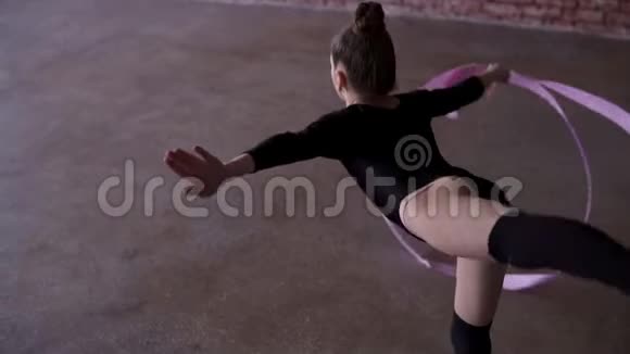 穿着黑色西装的小女孩在训练室用粉色丝带练习韵律体操动作背面录像视频的预览图