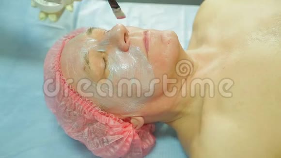戴手套的女美容师用刷子把治疗面具涂在男人的脸上视频的预览图