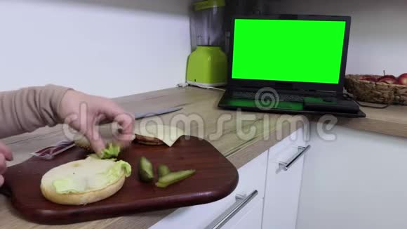 女人做汉堡看笔记本电脑绿色屏幕视频的预览图