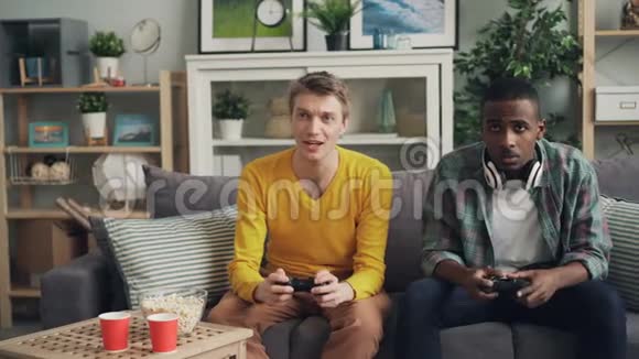 无忧无虑的男学生在家里的沙发上玩电子游戏操纵杆上的按钮集中在活动上视频的预览图
