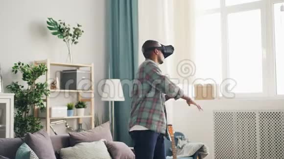 兴奋的年轻人正在玩游戏戴着虚拟现实眼镜在家里移动手臂和身体站在灯光室里视频的预览图