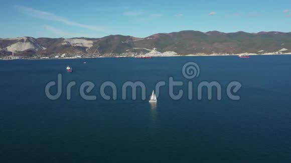 阳光明媚的白天白色帆船在海水上的空中镜头广视角视频的预览图