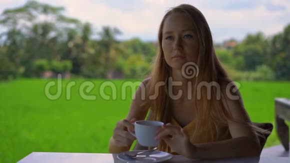 一位年轻女子在一家有稻田背景的乡村咖啡馆喝茶或咖啡的特写镜头视频的预览图