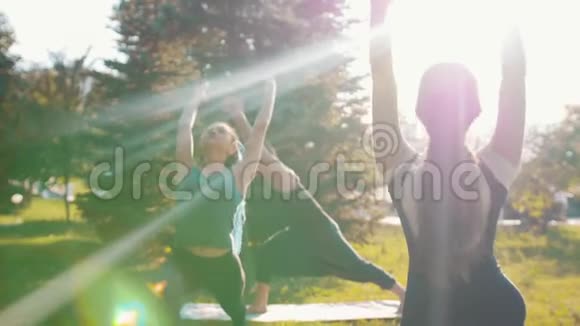 在阳光明媚的日子里两个年轻的女人和教练一起在公园里健身用腿做运动视频的预览图