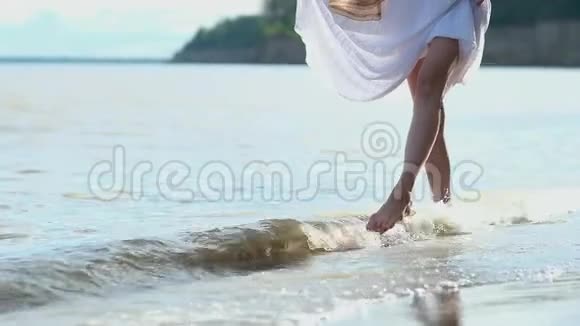 年轻苗条的女孩光着脚在海边的沙滩上行走牵手白色连衣裙在Shin和s上冲浪打女人视频的预览图