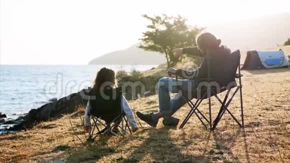 父亲和小女儿坐在湖边露营的椅子上后景视频的预览图