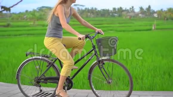 一个年轻的女人骑着自行车穿过美丽的稻田前往东南亚的概念慢镜头视频的预览图