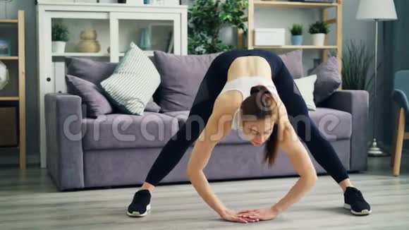 美丽的女孩在家锻炼弯曲向前伸展腿和背部视频的预览图