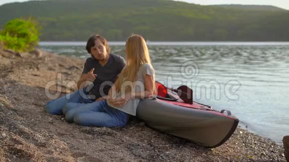 年轻的男人和女人坐在湖边或海滨的充气皮艇旁慢镜头视频的预览图