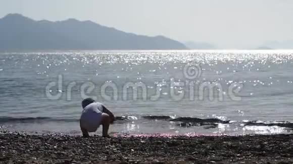 一个男孩慢吞吞地把一颗鹅卵石扔进阳光下灿烂的海水里视频的预览图