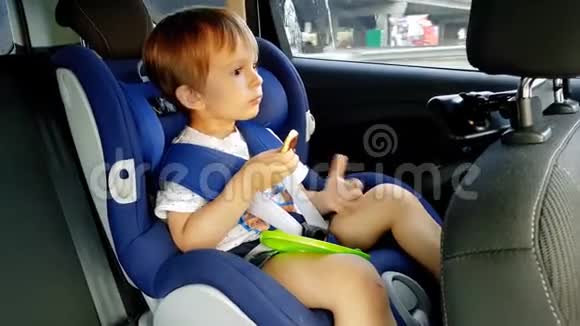 3岁幼儿男孩坐在儿童车安全座椅上吃东西的4镜头视频的预览图