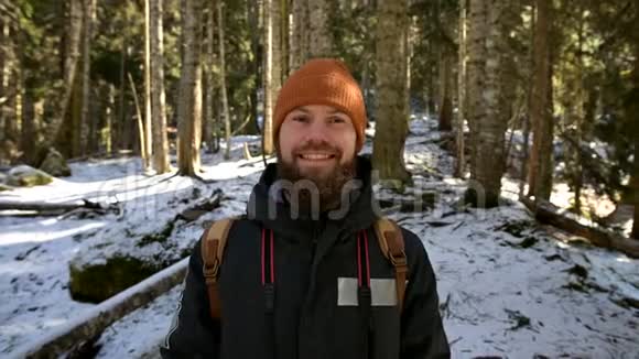 一个长着大胡子笑着的年轻人背着背包站在针叶林中的画像视频的预览图