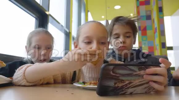 青少年朋友在披萨店边吃快餐边用手机看电影视频的预览图