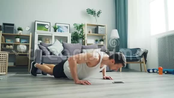 强壮健康的年轻人在地板上做俯卧撑看智能手机屏幕视频的预览图