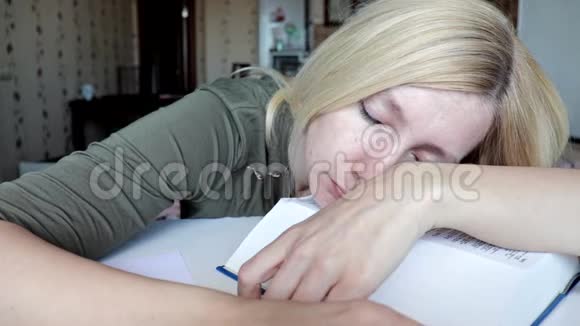 疲惫的女人坐在桌子旁睡觉头上戴着一本大书教育和学习观念视频的预览图