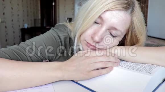 疲惫的女人坐在桌子旁睡觉头上戴着一本大书教育和学习观念视频的预览图