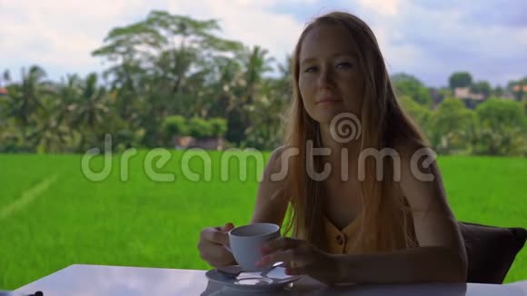一位年轻女子在一家有稻田背景的乡村咖啡馆喝茶或咖啡的特写镜头视频的预览图