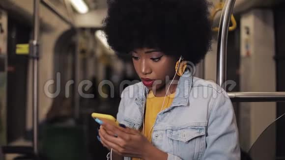严肃的非洲裔美国妇女戴耳机听音乐和在公共场合浏览手机的肖像视频的预览图